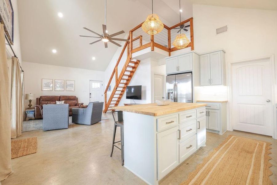 Kitchen with high vaulted ceiling, a center island, a kitchen bar, butcher block counters, and open floor plan