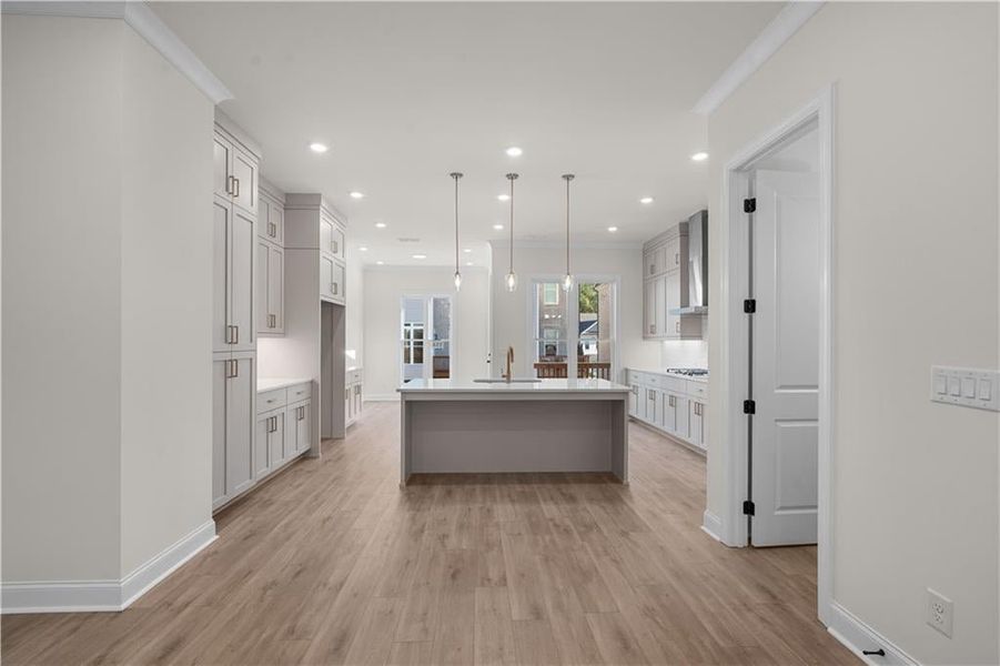 Kitchen featuring light wood-style flooring, a kitchen island with sink, pendant lighting, recessed lighting, and crown molding