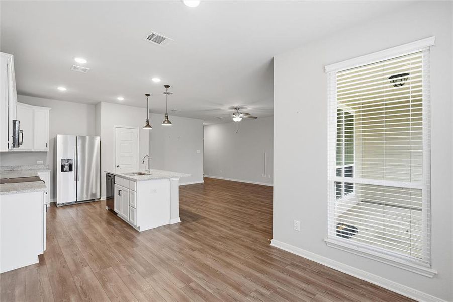 Kitchen featuring a center island with sink, hanging light fixtures, white cabinetry, open floor plan, and stainless steel fridge with ice dispenser