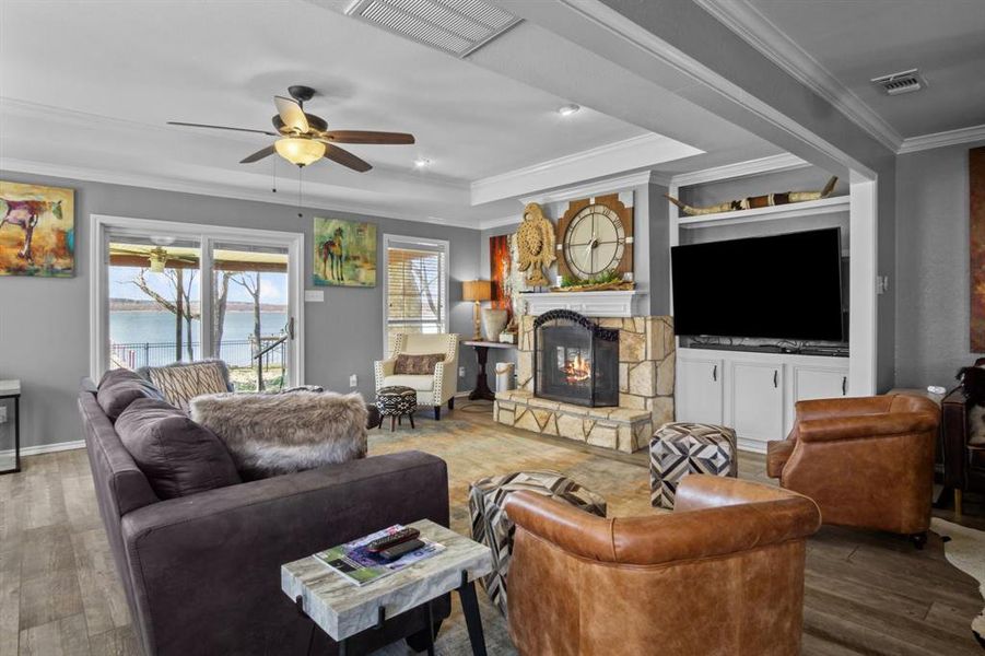 Living room featuring ornamental molding, a water view, a stone fireplace, and wood-type flooring