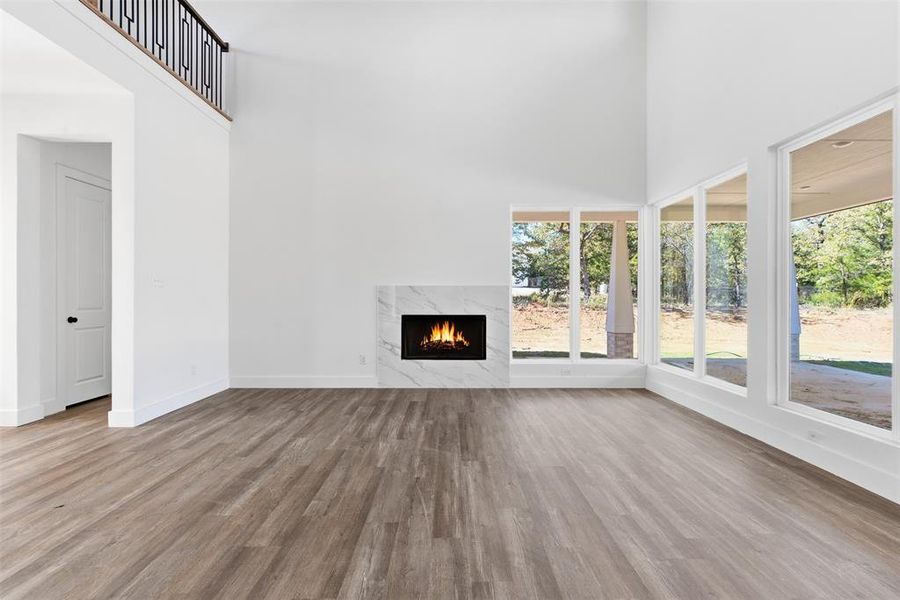 Unfurnished living room featuring a towering ceiling, light wood-style flooring, and a fireplace Unfurnished living room featuring a towering ceiling, light wood-style flooring, and a fireplace