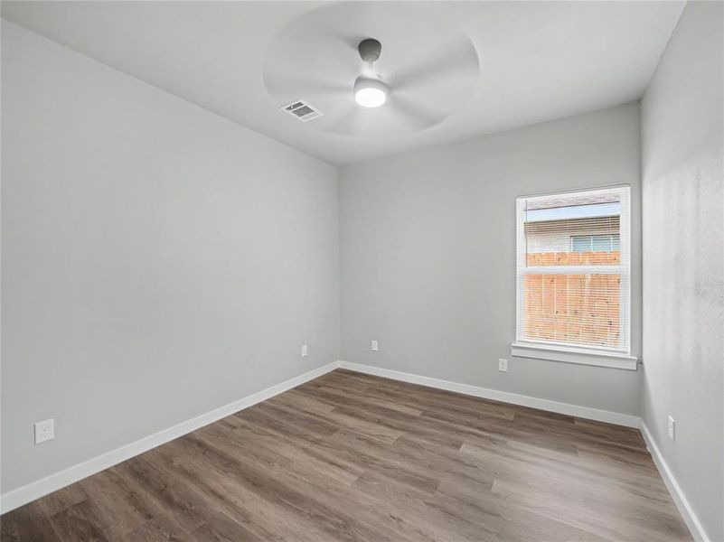 Room featuring wood-finish flooring, light gray walls, white trim, and a ceiling fan with integrated lighting Room featuring wood-finish flooring, light gray walls, white trim, and a ceiling fan with integrated lighting