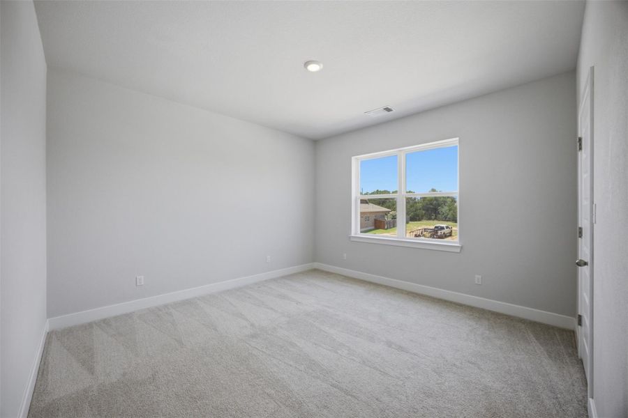 A well-lit bedroom features plush carpeting and a generous window overlooking the neighborhood.