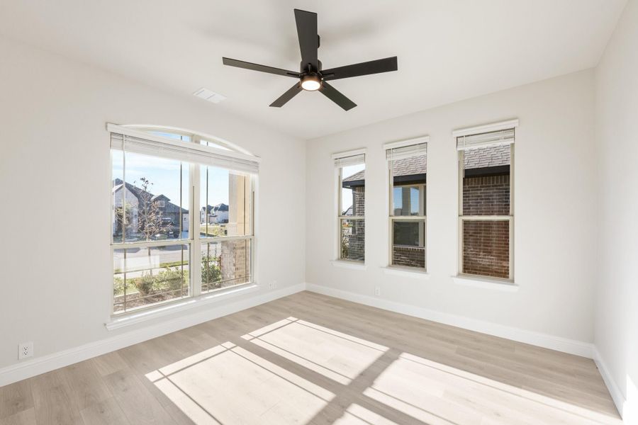 Empty room with light wood floors, ceiling fan, and large windows with neighborhood view Empty room with light wood floors, ceiling fan, and large windows with neighborhood view
