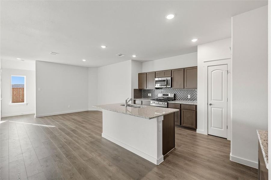 Kitchen featuring a kitchen island with sink, light stone counters, appliances with stainless steel finishes, tasteful backsplash, and dark wood-style floors Kitchen featuring a kitchen island with sink, light stone counters, appliances with stainless steel finishes, tasteful backsplash, and dark wood-style floors