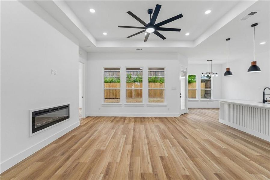 Spacious living area featuring wood-finish flooring, a linear electric fireplace, and a large ceiling fan with multiple blades Spacious living area featuring wood-finish flooring, a linear electric fireplace, and a large ceiling fan with multiple blades