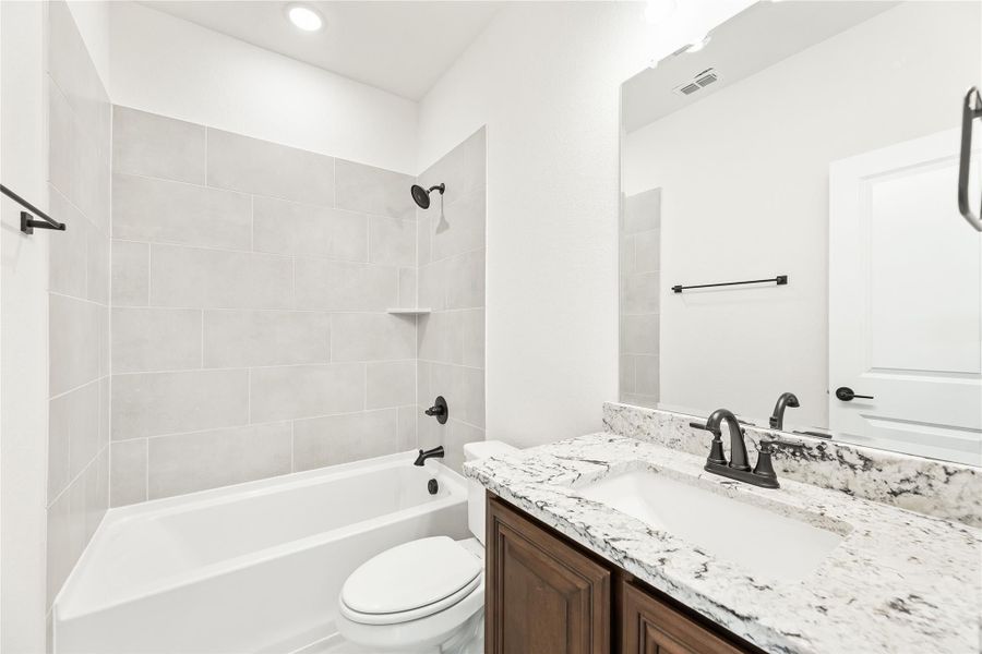 Bathroom with tiled tub-shower combo, dark wood vanity, granite countertop, and black fixtures Bathroom with tiled tub-shower combo, dark wood vanity, granite countertop, and black fixtures