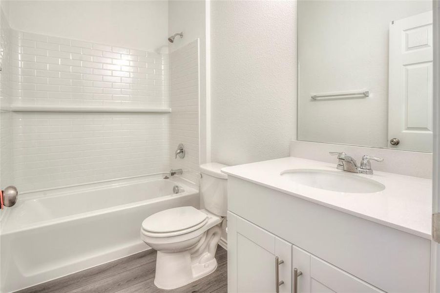 Bathroom featuring vanity, shower / bathtub combination, wood finished floors, and a textured wall Bathroom featuring vanity, shower / bathtub combination, wood finished floors, and a textured wall