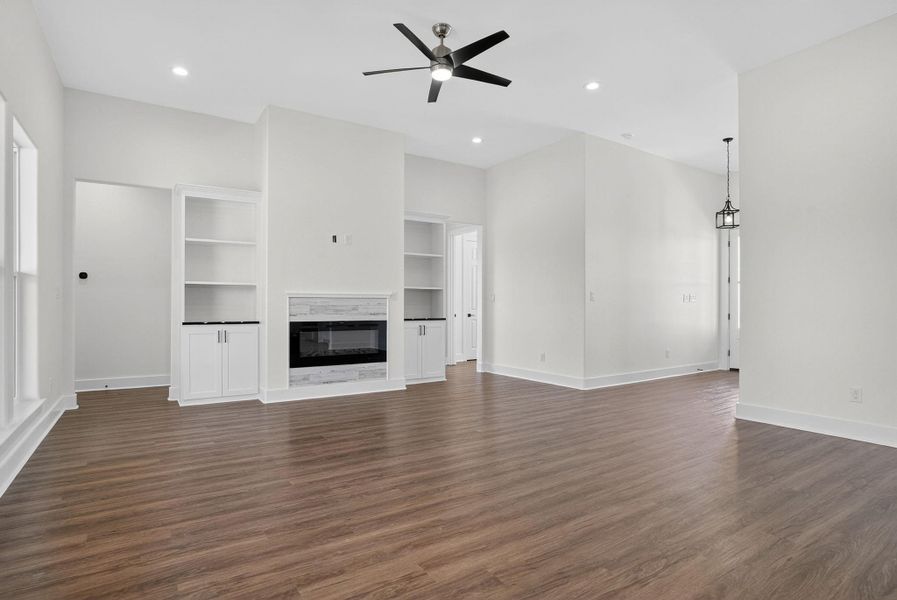 Unfurnished living room with a glass covered fireplace, dark wood-style floors, built in shelves, recessed lighting, and a ceiling fan Unfurnished living room with a glass covered fireplace, dark wood-style floors, built in shelves, recessed lighting, and a ceiling fan