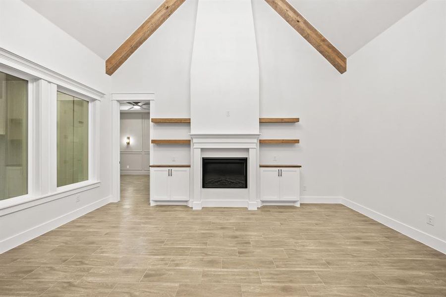 Spacious room featuring vaulted ceilings with exposed wood beams, a fireplace with a mantel, built-in cabinetry with wood countertops, and large windows