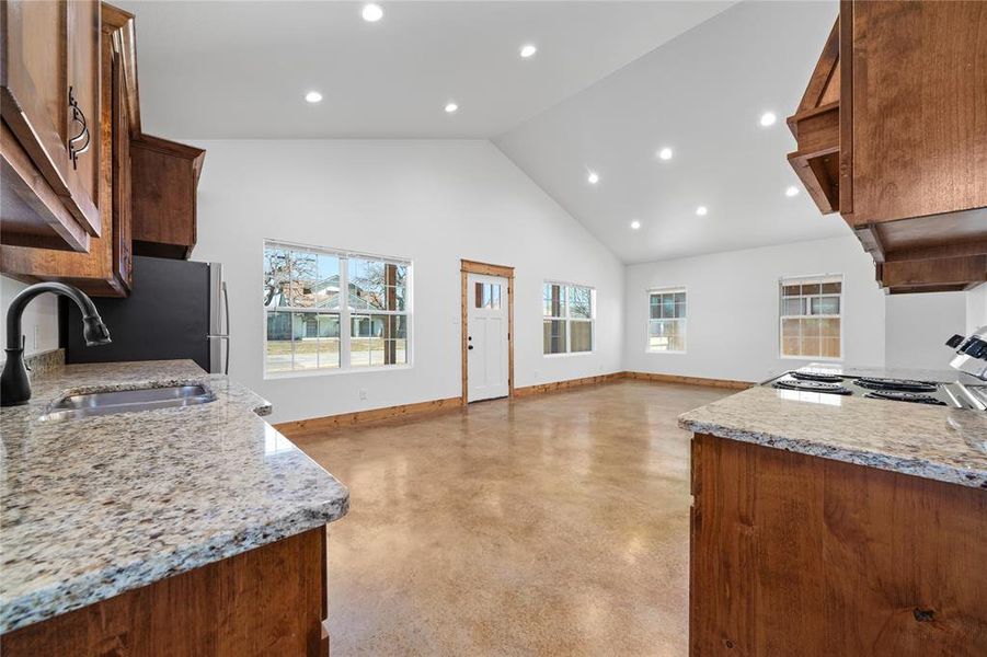 Kitchen featuring high vaulted ceiling, baseboards, electric stove, a sink, and light stone countertops Kitchen featuring high vaulted ceiling, baseboards, electric stove, a sink, and light stone countertops