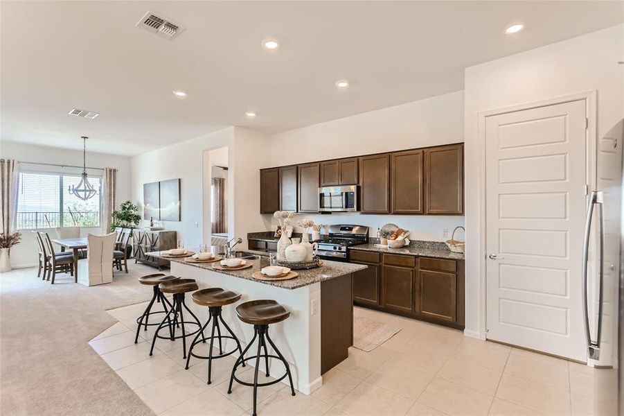 Kitchen with light stone countertops, a kitchen breakfast bar, a kitchen island with sink, appliances with stainless steel finishes, and recessed lighting