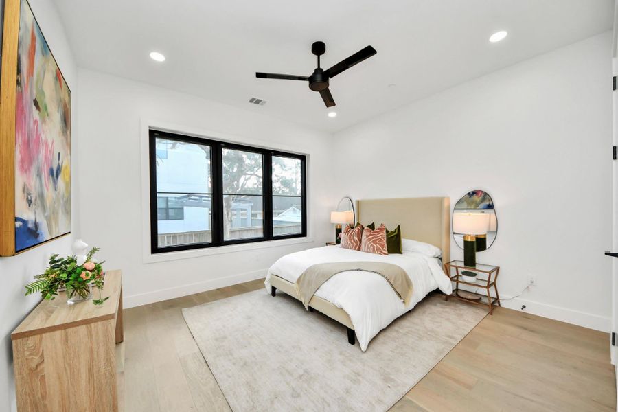 Bright and inviting, the first-floor primary/guest suite blends modern elegance with functionality, where light-filled windows and a bold black ceiling fan create a sophisticated sanctuary.