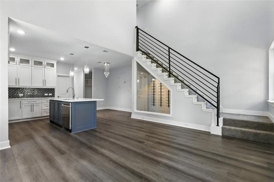 Kitchen with dark wood-style flooring, white cabinetry, an island with sink, glass insert cabinets, and decorative backsplash