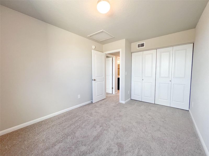 Unfurnished bedroom with attic access, a closet, and carpet