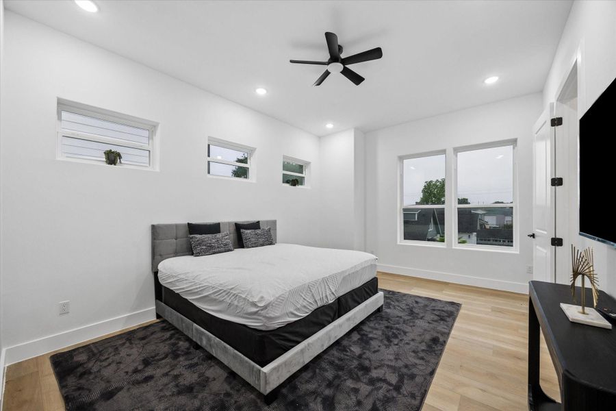 This bedroom features a modern design with clean lines, large windows for natural light, a ceiling fan, and recessed lighting. The room has a spacious feel with light wood flooring and a cozy area rug. This bedroom features a modern design with clean lines, large windows for natural light, a ceiling fan, and recessed lighting. The room has a spacious feel with light wood flooring and a cozy area rug.