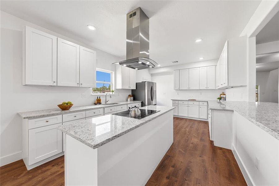 Modern kitchen featuring an expansive center island with an integrated cooktop and stainless steel range hood