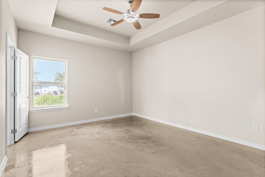 Unfurnished bedroom with concrete floors, a raised ceiling, and a ceiling fan