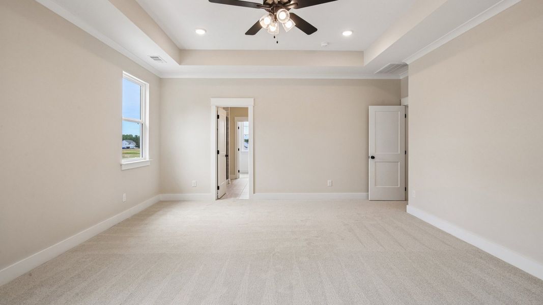 Primary suite with tray ceiling, ceiling fan, and carpet Primary suite with tray ceiling, ceiling fan, and carpet