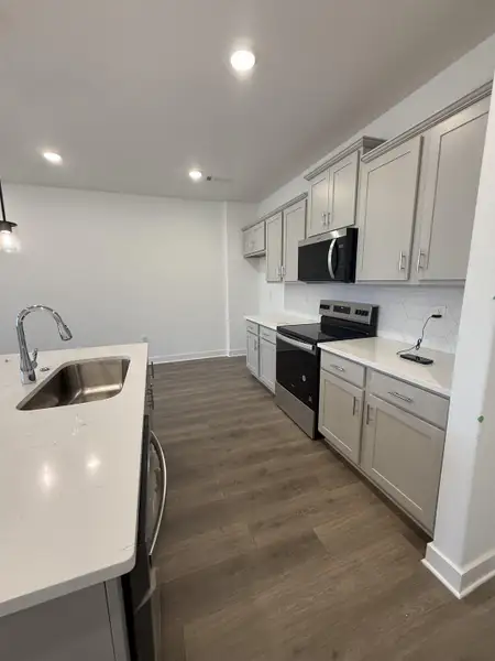Kitchen with stainless steel appliances, gray cabinets, dark wood-style floors, tasteful backsplash, and light stone countertops