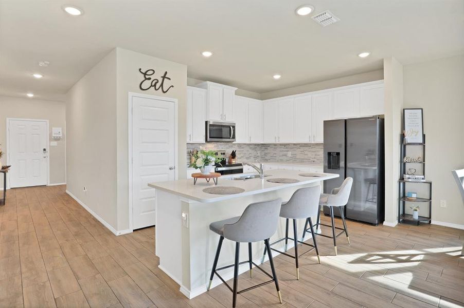 Kitchen featuring stainless steel appliances, a breakfast bar, white cabinets, a center island with sink, and light wood-type flooring