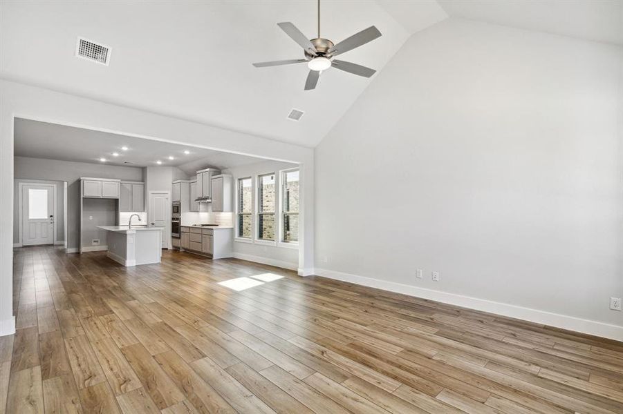 Unfurnished living room featuring high vaulted ceiling, light hardwood / wood-style flooring, ceiling fan, and sink