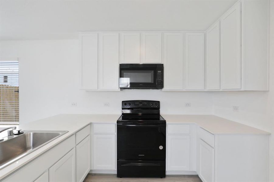 Modern kitchen featuring white shaker-style cabinetry, a stainless steel double-basin sink, black electric range, and an integrated black microwave