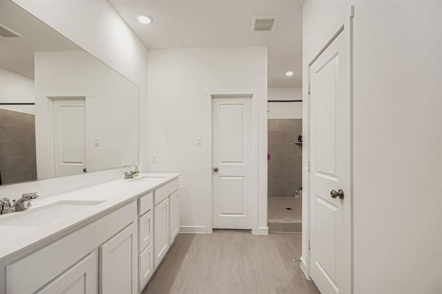 Bathroom with double vanity, light wood-style flooring, tiled shower, and recessed lighting
