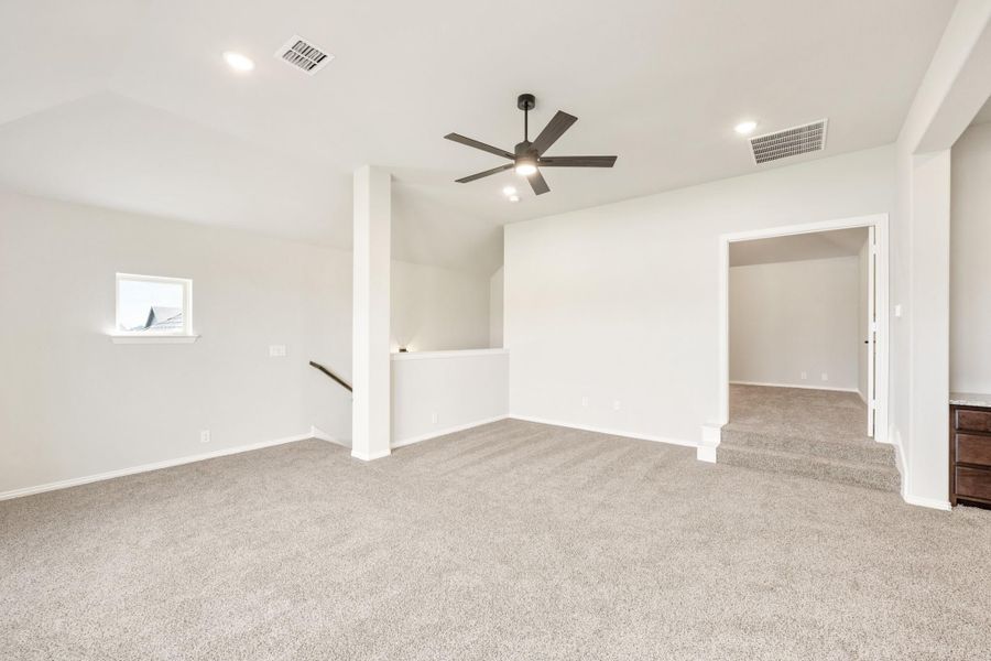 Spacious open room with gray carpet, ceiling fan, white walls, and staircase opening Spacious open room with gray carpet, ceiling fan, white walls, and staircase opening