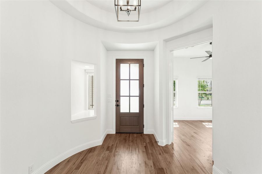 Rounded entryway with wood front door, tray ceiling, pendant light, and hardwood floors