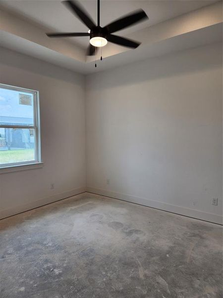 Unfurnished room featuring ceiling fan, a raised ceiling, and concrete floors