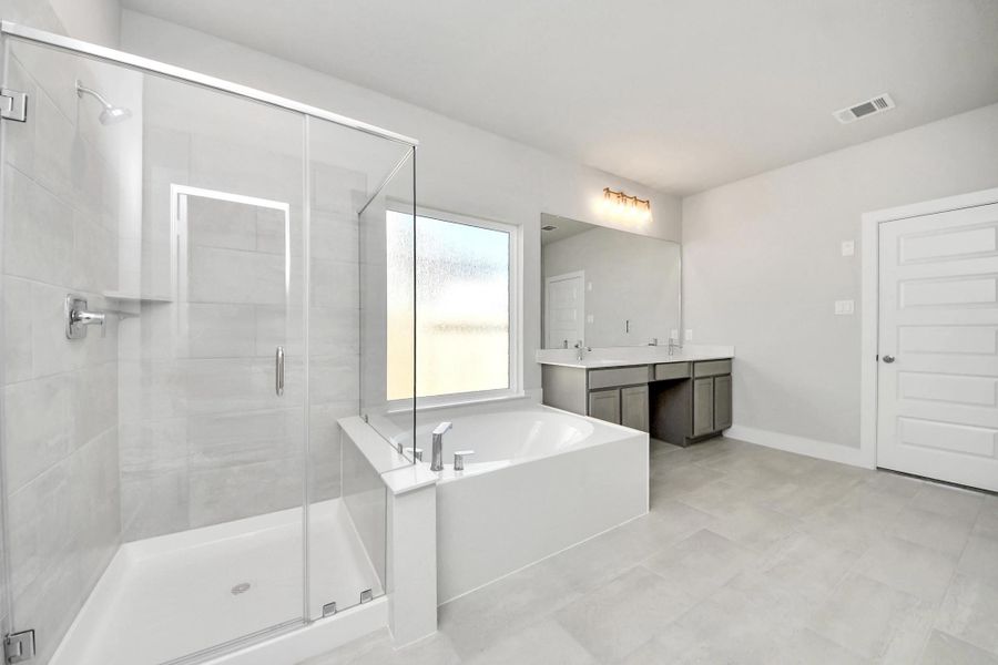 Escape to a spa-like oasis in this primary bathroom. Enjoy a walk-in shower with tile surround, a separate garden tub with custom detailing, and an elegant vanity featuring light countertops, modern hardware, and beautiful vanity lights. Experience luxury and relaxation in every detail.