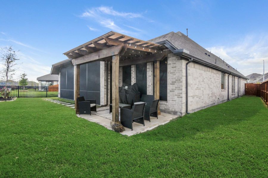 This photo showcases the homes modern exterior with a well-maintained lawn and a cozy patio area. The patio features a pergola for shade and seating, perfect for outdoor relaxation or entertaining. The house has a brick facade and a fenced yard, offering privacy and charm.