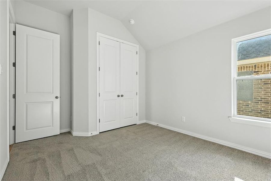 Unfurnished bedroom featuring light carpet, lofted ceiling, and a closet