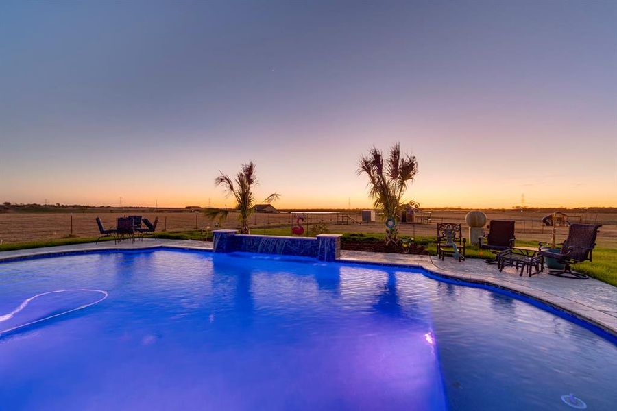 Pool at dusk with pool water feature and a patio