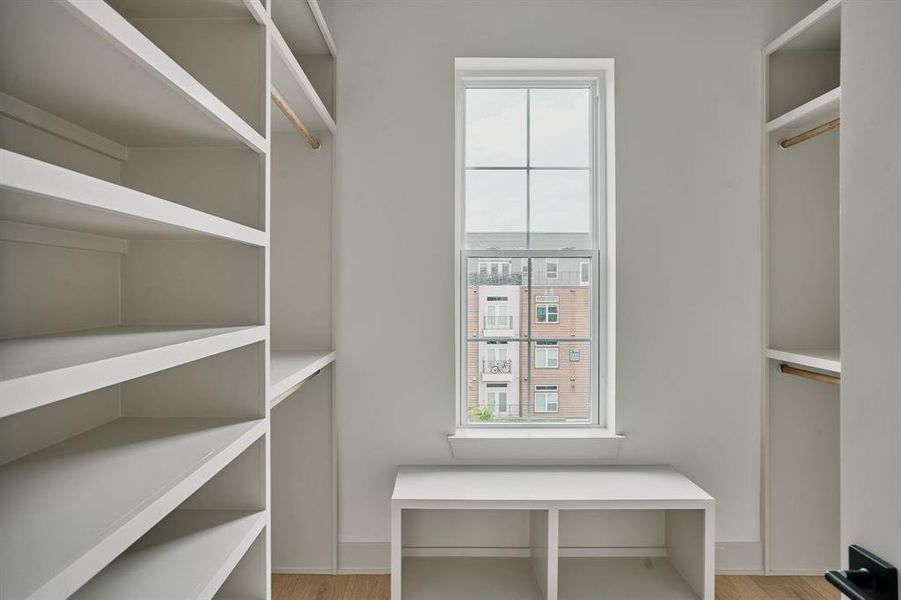 Walk-in closet featuring extensive built-in shelving, hanging rods, an integrated storage bench, a window, and wood-finish flooring Walk-in closet featuring extensive built-in shelving, hanging rods, an integrated storage bench, a window, and wood-finish flooring