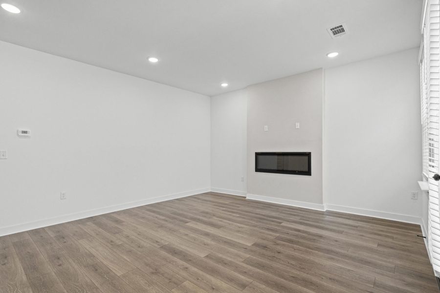 Room featuring a linear fireplace, wood-finish flooring, recessed lighting, and white baseboards