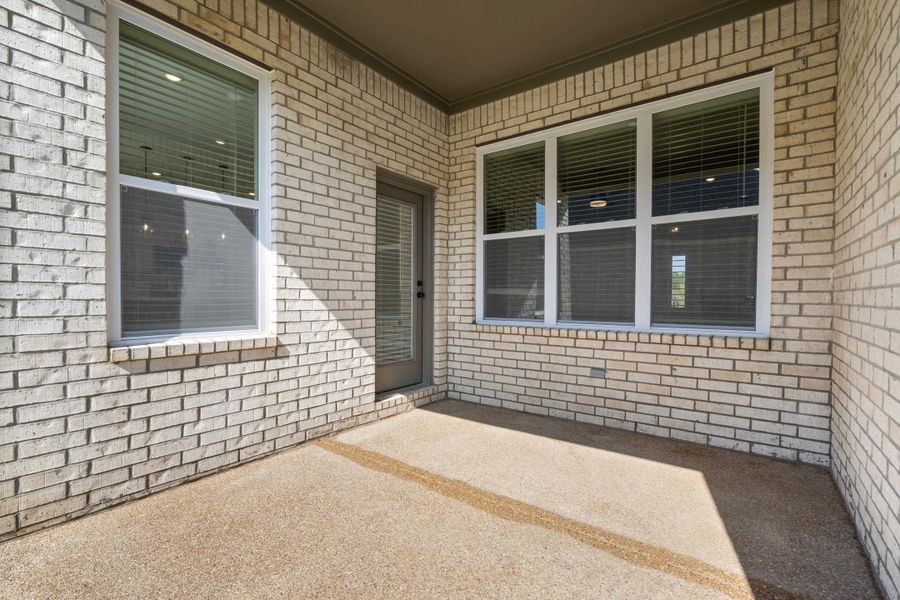 Covered patio featuring a brick exterior, a single entry door with an integrated window, and multiple large windows with white frames Covered patio featuring a brick exterior, a single entry door with an integrated window, and multiple large windows with white frames