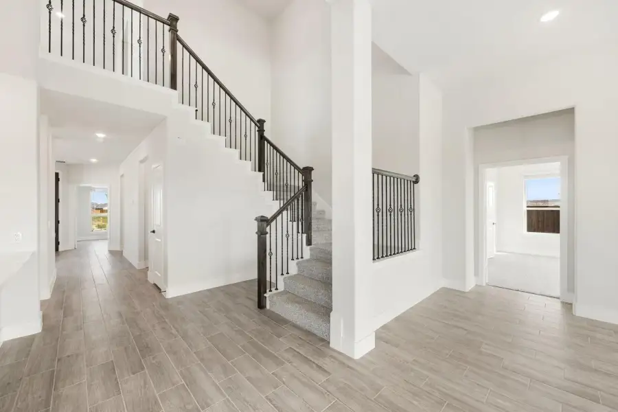 Two-story entryway with carpeted staircase, wrought iron balusters, and wood-look tile floors