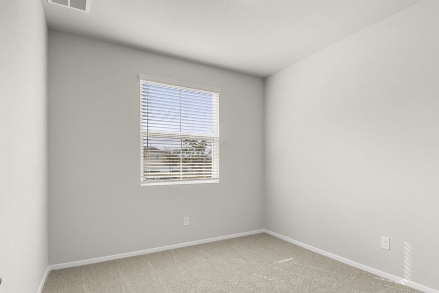 Image of a bedroom with tan carpeting with light grey walls and a window