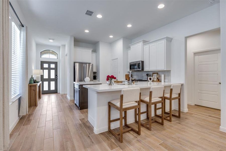 Kitchen with white cabinets, backsplash, a peninsula, a kitchen breakfast bar, and stainless steel appliances
