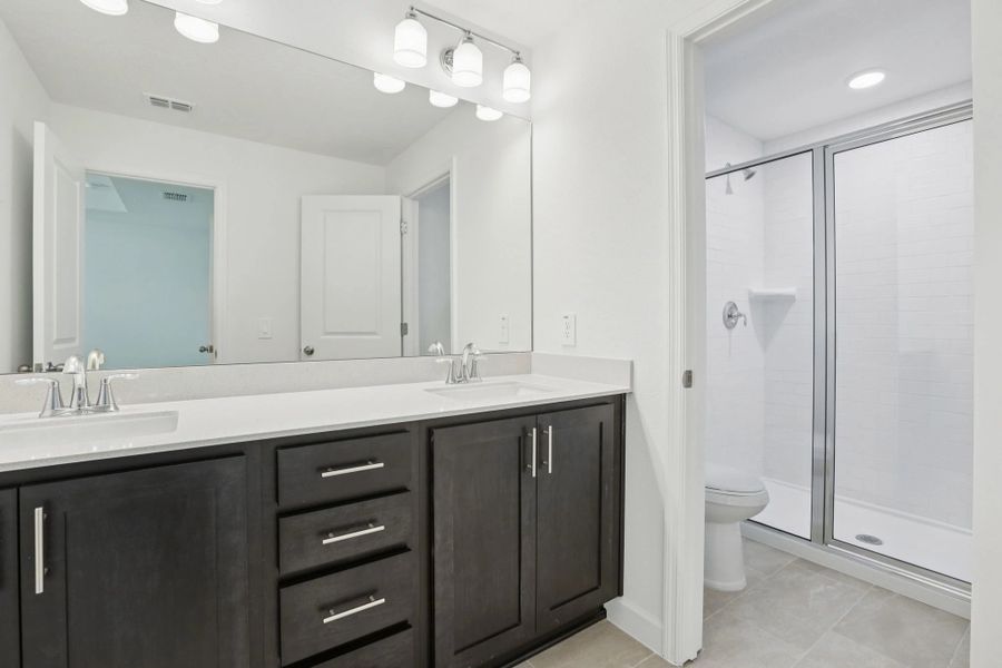 Luxurious primary bath features dual vanities and a stunning glass walk-in shower