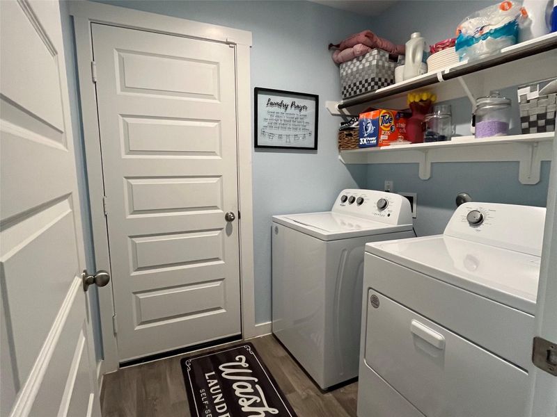 This photo shows a compact, organized laundry room , shelving for storage, and a clean, modern design. The space features light blue walls, white doors, and wood-look flooring, creating a fresh and functional environment.