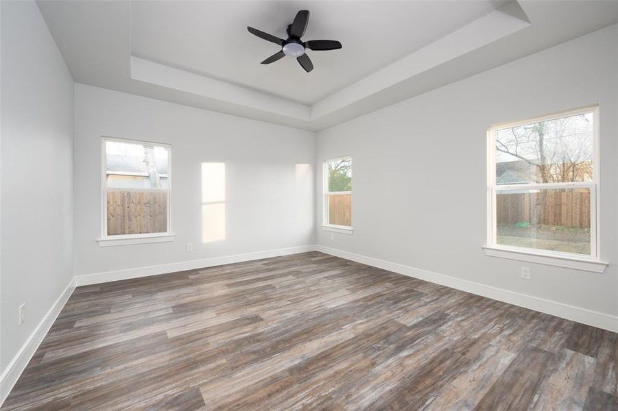 Unfurnished room with a tray ceiling, dark wood-style floors, and ceiling fan