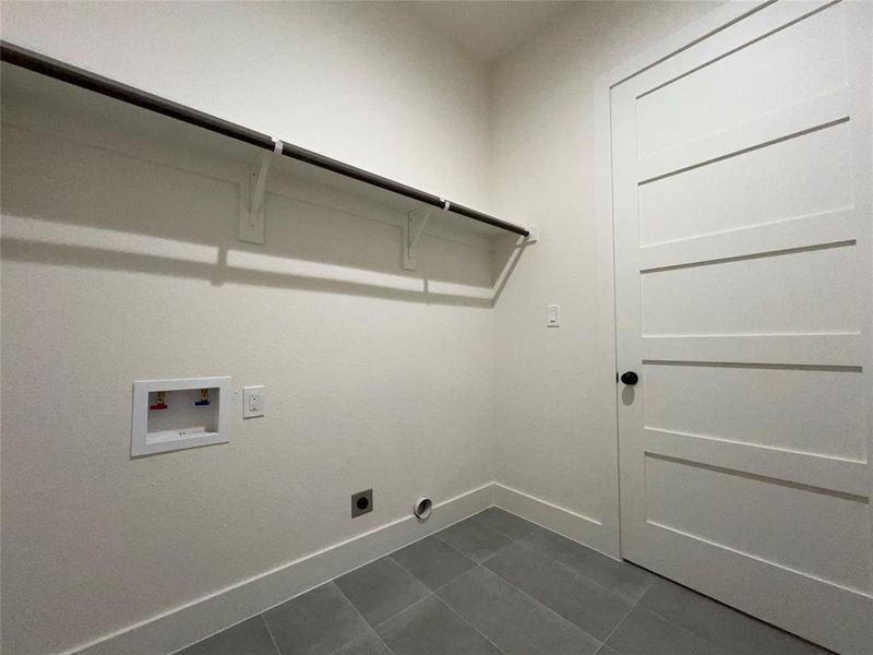 Laundry area featuring a hanging rod, modern panel door with black hardware, and gray tile flooring