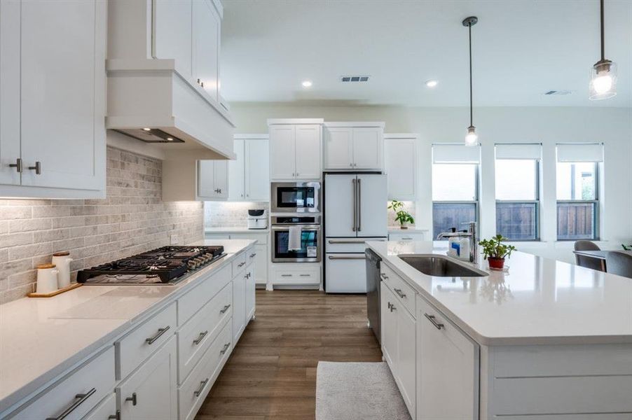 Kitchen with white cabinetry, appliances with stainless steel finishes, light stone countertops, pendant lighting, and backsplash Kitchen with white cabinetry, appliances with stainless steel finishes, light stone countertops, pendant lighting, and backsplash