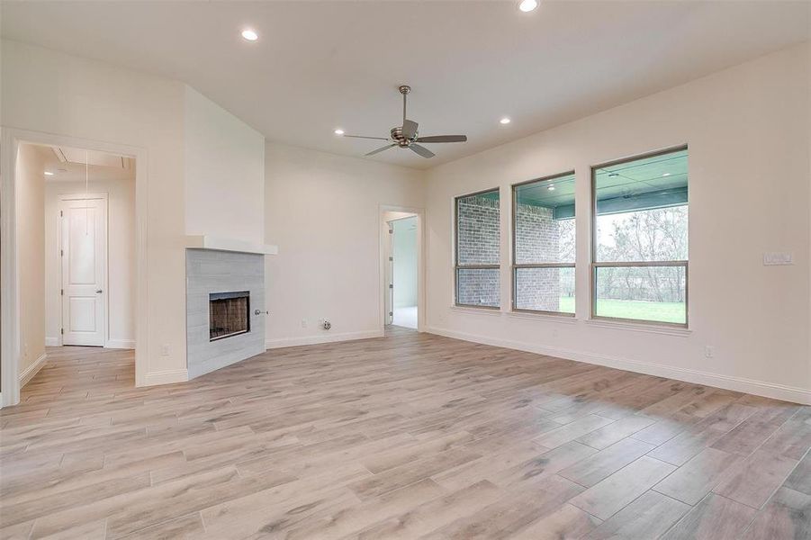 Unfurnished living room featuring light wood-type flooring, a tiled fireplace, and ceiling fan