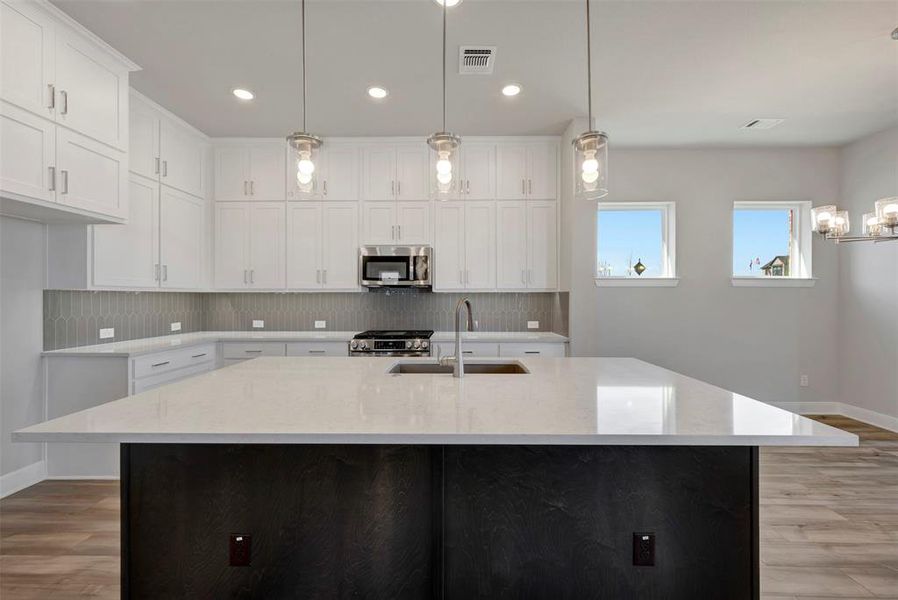 Kitchen with light wood finished floors, light stone countertops, decorative light fixtures, stainless steel appliances, and two tone color scheme