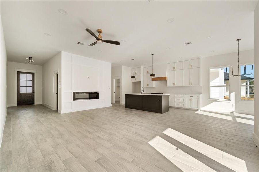 This spacious living area features 6 recessed lights, a ceiling fan, modern gold and black light fixtures, and a custom accent wall with a fireplace that adds a touch of elegance and sophistication. The room is beautifully finished with wood look tile flooring!