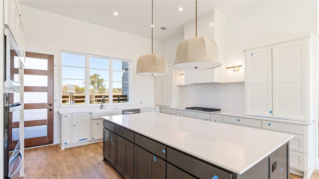 Kitchen featuring pendant lighting, white cabinets, sink, light hardwood / wood-style floors, and a kitchen island